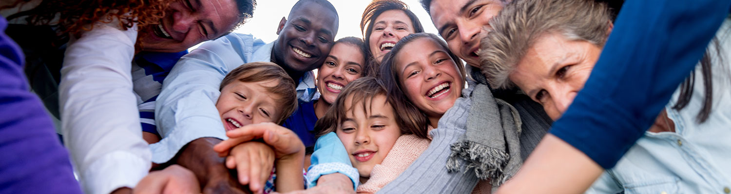 Adults and children huddle together and put their hands together in a pile while smiling and laughing