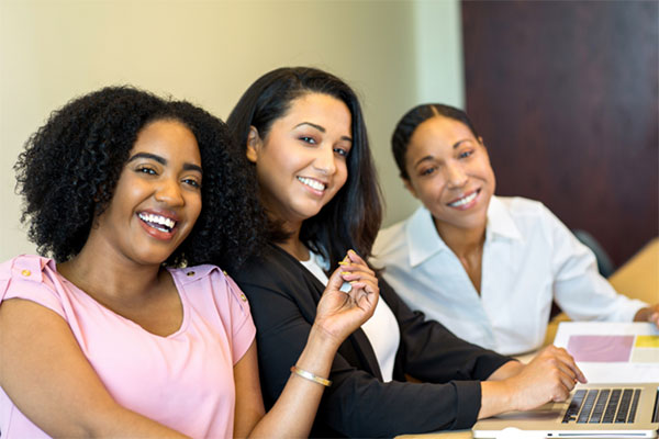 3 women smiling for a picture as they sit together during an office meeting