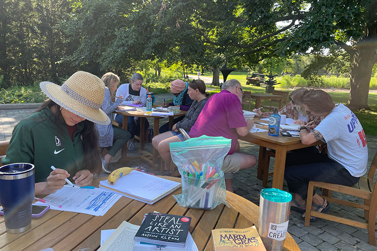 Summer institute participants work on their writing while enjoying the outdoor scenery at Lynden Sculpture Garden on a sunny day.