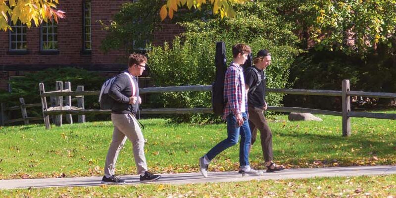 Three male students walking across campus in fall.