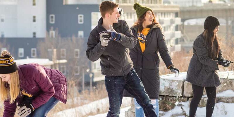 Students (white woman, man and Asian women) throwing snowballs in Milwaukee.