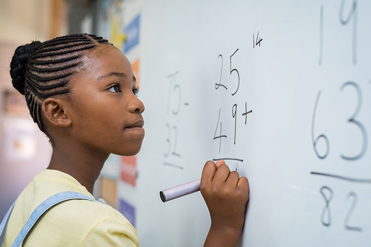 A student (african american female) working through a math equation on her classroom whiteboard