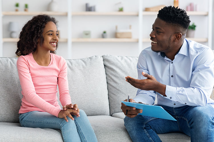 A counselor (african american man) having a happy conversation with a young female patient (african american girl)