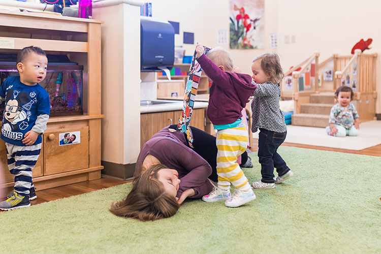 A teacher (white woman) plays with infant children at day care