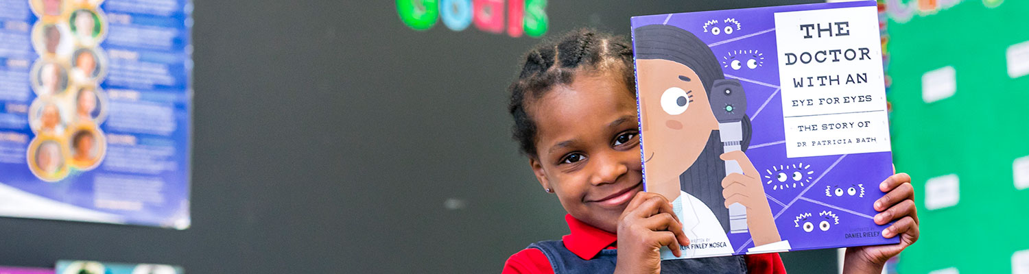 Young student (african american girl) holding a book up while smiling for the camera