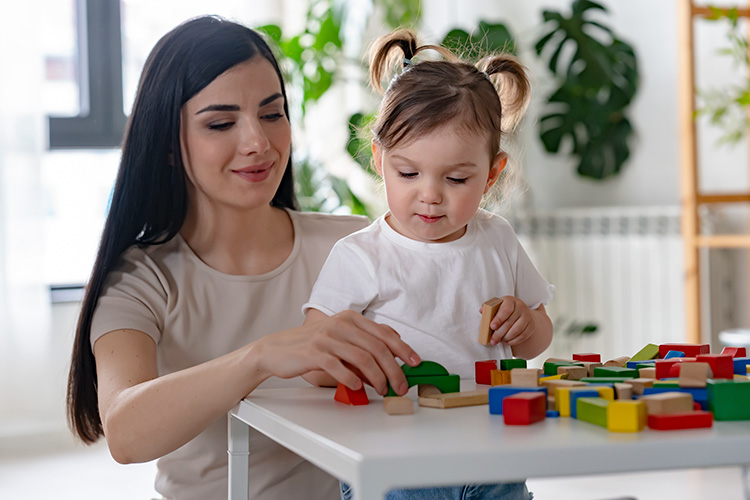 Female early childhood education teacher working with building blocks at a table with a young child.
