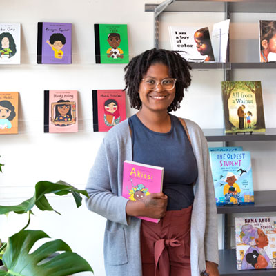 School of Education alumna Ashley Valentine, poses for a picture inside of her bookstore and tutoring center named Rooted MKE.