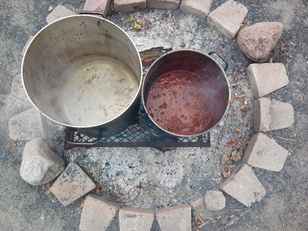 image of two large pots with liquid soup over a fire that is surrounded by cut stones