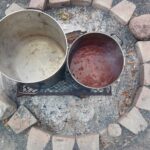 image of two large pots with liquid soup over a fire that is surrounded by cut stones