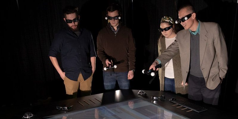 Three students and professor gather around virtual reality table