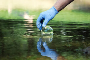 gloved hand getting water sample from green water