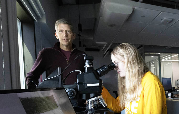 a male civil engineering faculty member and a woman who is looking at a microscope