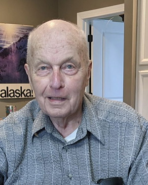 A bald man wearing a gray collared shirt looks at the camera.