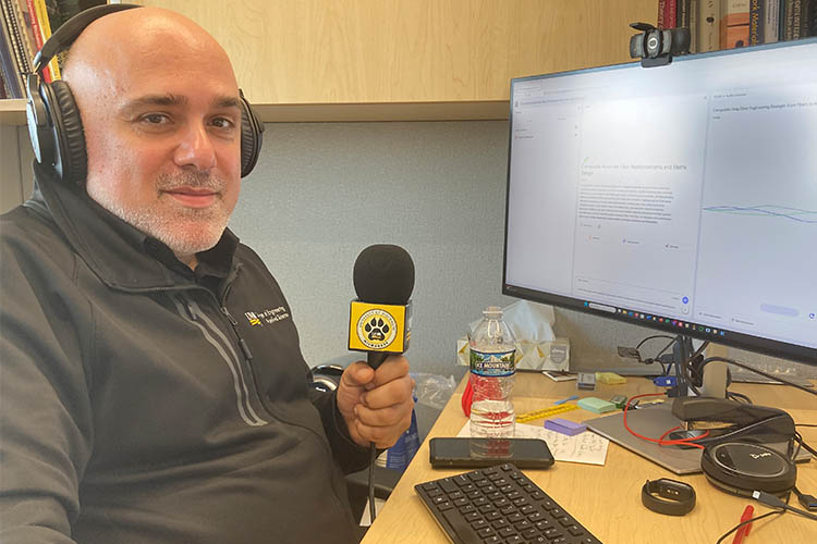 a man with a microphone wearing headphones in front of a computer screen looks at the camera