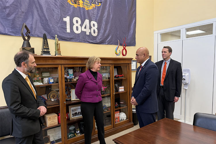 Three men in dark suit jackets and one women in a purple jacket talk among themselves.