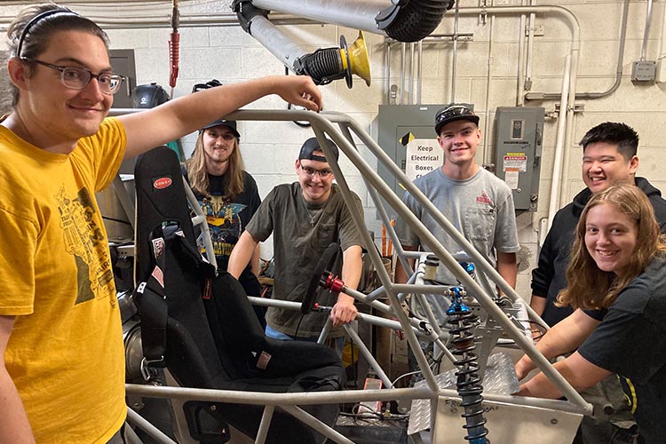 Six students, including one woman, far right, display the Baja car they're working on.