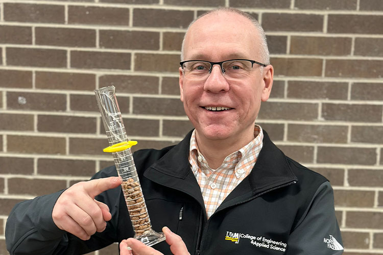 A man with glasses holds a test tube filled with beans.