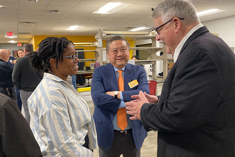 An African-American woman, left, speaks with a middle-age man with glasses, right. An Asian man with glasses stands between them listening to the conversation.