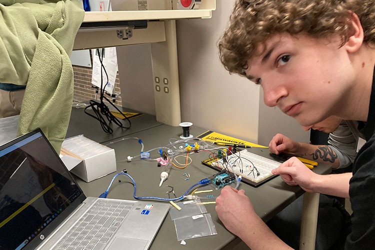 Close up shot of a young man with sandy, curly hair who is working on building a circuit board.