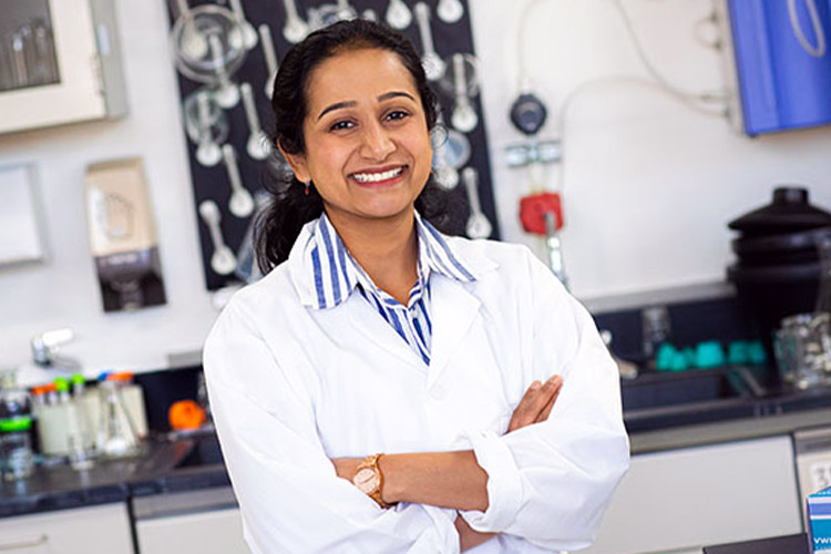 A woman with dark hair and wearing a white lab coat, smiles at the camera.