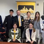 A group portrait of nine people, four women and five men. All are Chinese college students except the dean, standing third from the left in a gold tie.