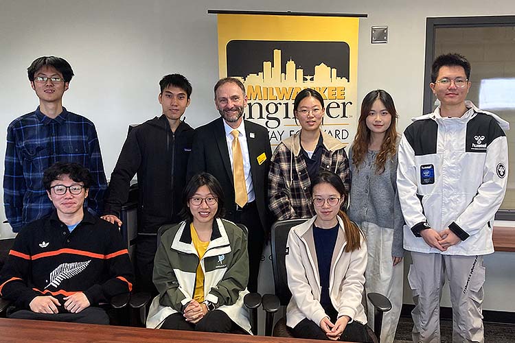 A group portrait of nine people, four women and five men. All are Chinese college students except the dean, standing third from the left in a gold tie.