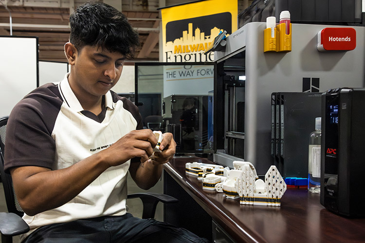 a young man wearing a black and white hoodie inspects some 3D printed pieces for a robot.
