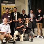 A group shot of 10 people each holding an awards plaque. The three in front are on one knee.