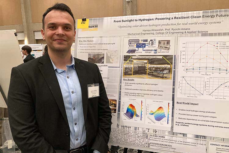A man with short dark hair, dark jacket and light blue shirt poses with an engineering research poster to one side.