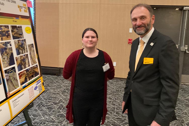 A young woman shows her engineering research poster to a male judge.