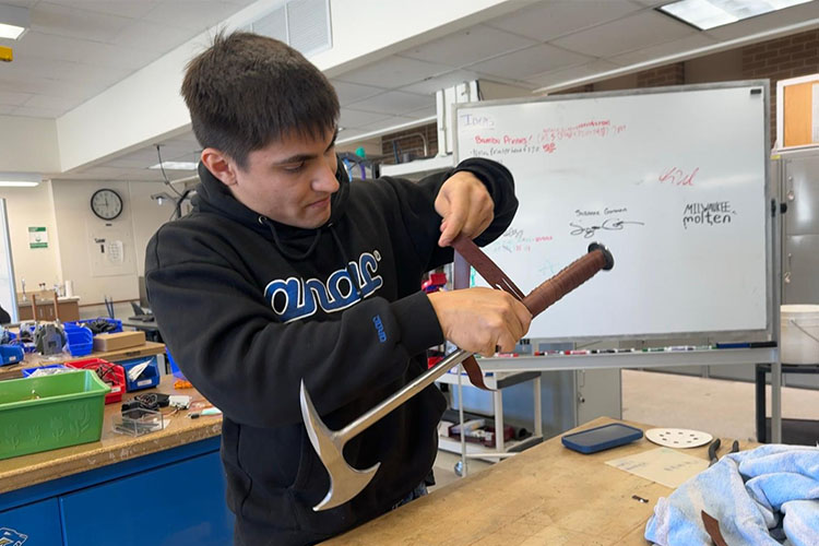Young man in dark hoodie wraps a small metal axe with a leather strip.