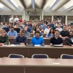 A large group of college students look at the camera. All are seated in rows.