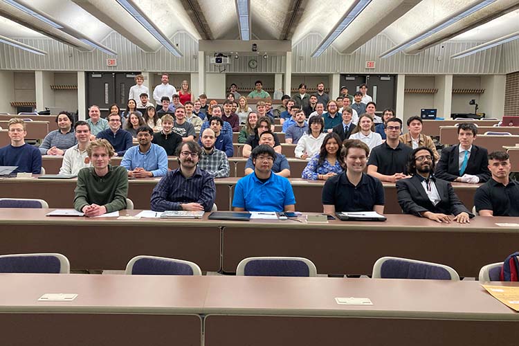 A large group of college students look at the camera. All are seated in rows.