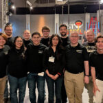 Eleven people pose for a group shot. A TV studio is behind them.