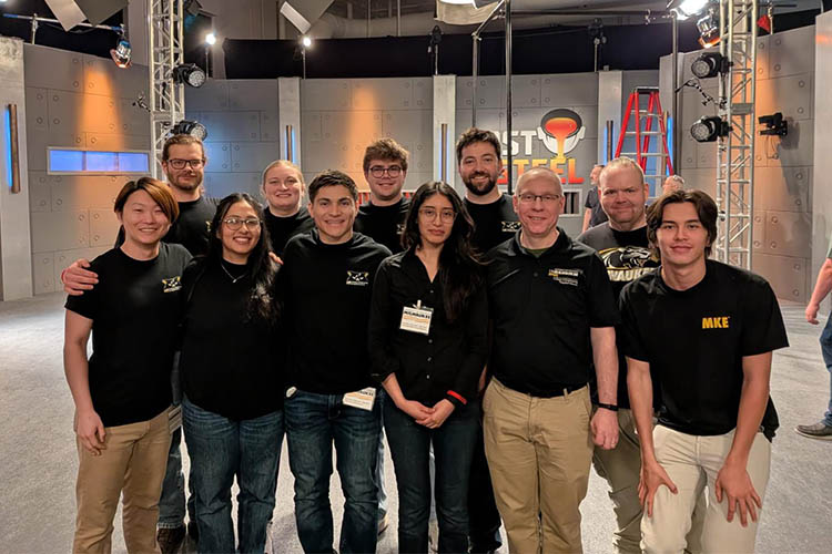Eleven people pose for a group shot. A TV studio is behind them.