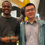 Two men display a small glass award. Both are looking at the camera.