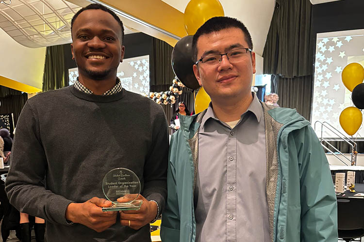 Two men display a small glass award. Both are looking at the camera.