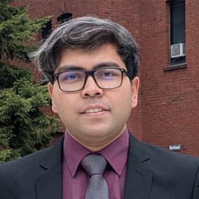 head and sholders shot of a man with dark hair and glasses, wearing a purple shirt and dark jacket/tie.
