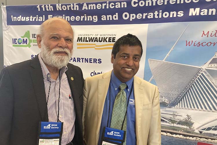 Two men in suits standing side by side looking at the camera. Man on the left has a gray beard. Man on the right is wearing a cream-colored jacket. Two men in suits standing side by side looking at the camera. Man on the left has a gray beard. Man on the right is wearing a cream-colored jacket.