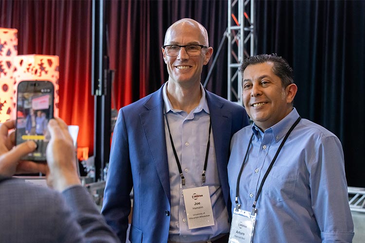 Two men pose for photos. The one on the left is bald and has glasses. The one on the right is wearing a light blue button-down shirt. Two men pose for photos. The one on the left is bald and has glasses. The one on the right is wearing a light blue button-down shirt.