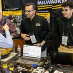 Two men in black shirts greet visitors to the UWM energy audit booth at an engineering summit.