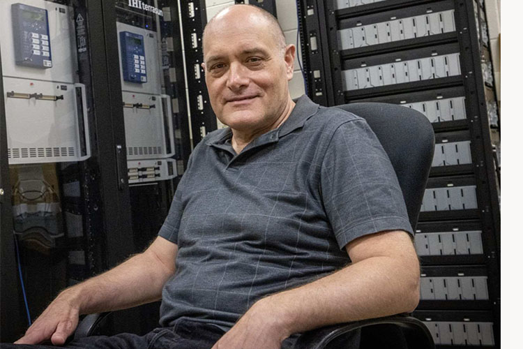 A seated man in a gray polo shirt looks at the camera.