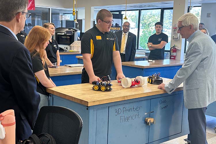 A young man talks to an older man. On the table between them are 3D printed toys.