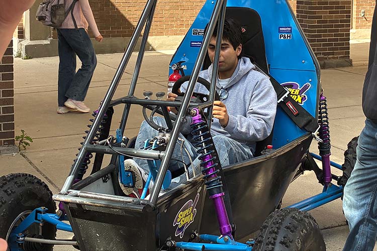 A young man with dark hair sits in the driver's seat of a Baja off-road vehicle. A young man with dark hair sits in the driver's seat of a Baja off-road vehicle.