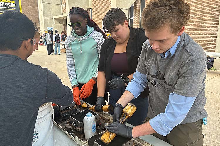Two young women on the left and a man stand next to each other while they participate in a metalcasting exercise. Two young women on the left and a man stand next to each other while they participate in a metalcasting exercise.