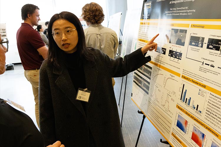 A young Asian woman points to a poster while she speaks to a guest on her other side.