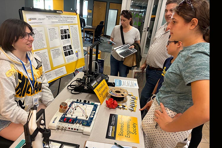 A young woman, left, shows three visitors a prototype biomedical 3D printer.