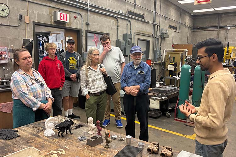 A group of eight people gather around a table displaying metal parts.