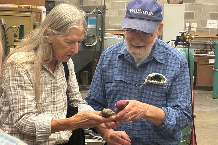 An older couple, woman on the left and man in a cap inspect a cast metal object.
