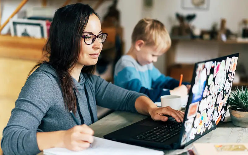 Young woman working on a laptop while her child sits nearby